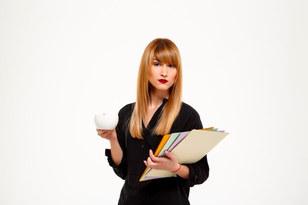 Successful businesswoman holding folders and cup over white wall