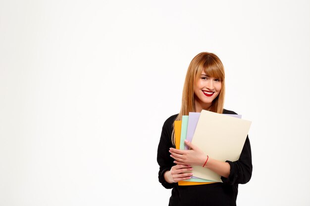Successful businesswoman holding folders and smiling over white wall Copy space.