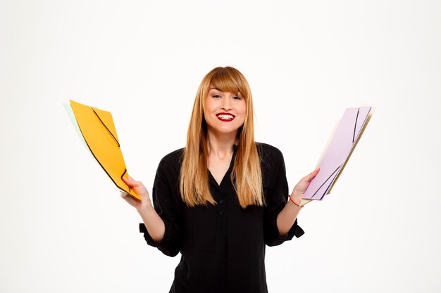 Successful businesswoman holding folders and smiling over white wall