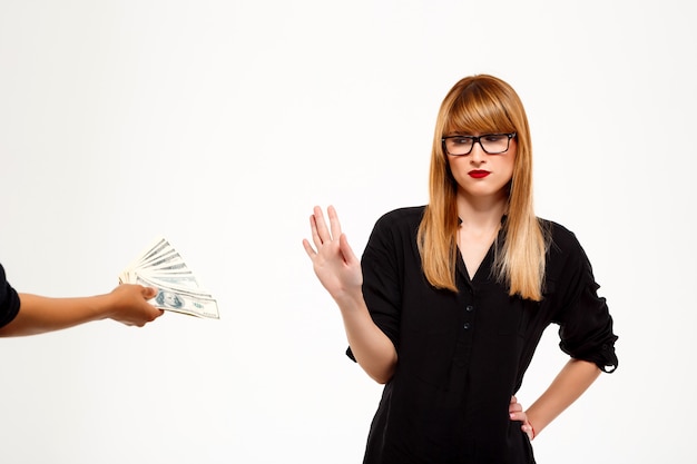 Successful businesswoman refusing of money over white wall