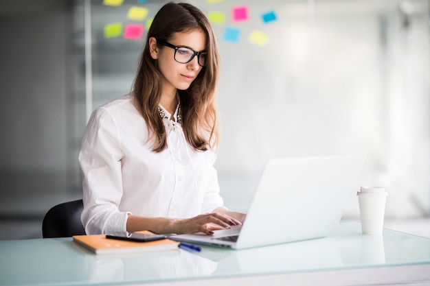 Successful businesswoman working on laptop computer in her office dressed up in white clothes