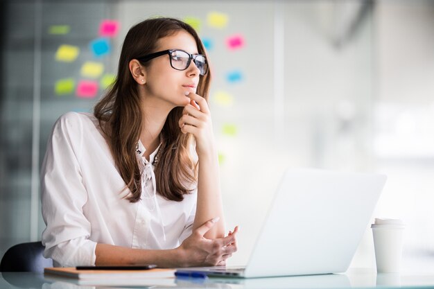 Successful businesswoman working on laptop computer and thinks on new ideas in her office dressed up in white clothes