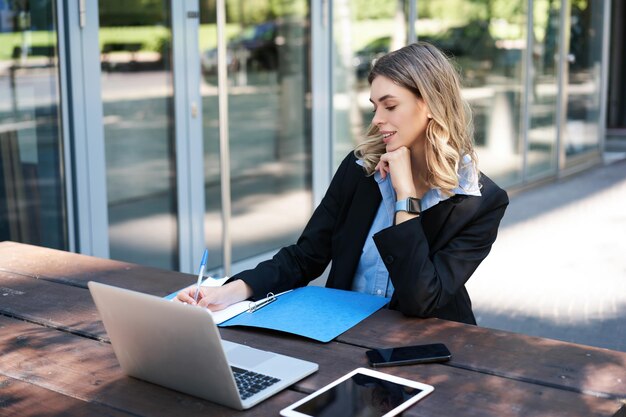 Успешная деловая женщина, работающая на открытом воздухе, корпоративная женщина, сидящая на скамейке с ноутбуком и пишущая