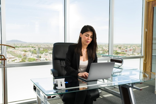 Успешная и занятая женщина-босс, усердно работающая для достижения своих бизнес-целей, печатая на своем ноутбуке за современным офисным столом