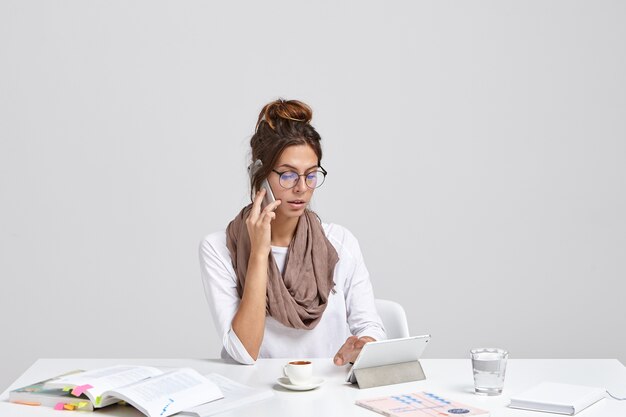 Successful busy prosperous businesswoman checks notes on touch pad while calls via smat phone