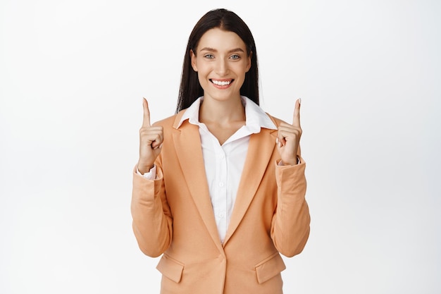 成功した企業の女性は笑顔で指を指して、白い背景の上に立って広告会社のブランド名を上向きに表示します