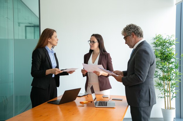 Successful coworkers talking, holding papers and working together