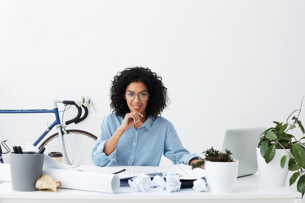 Successful dark-skinned woman engineer in formal wear holding pen while drawing