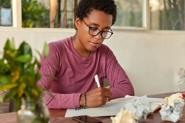 Foto gratuita designer di successo con la pelle nera, taglio di capelli da ragazzo, scrive il piano per la settimana su carta bianca