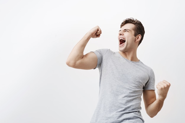 Free photo successful emotional young caucasian male sportsman with dark hair screaming yes and raising clenched fists in the air, feeling excited. people, success, triumph, victory, winning and celebration.