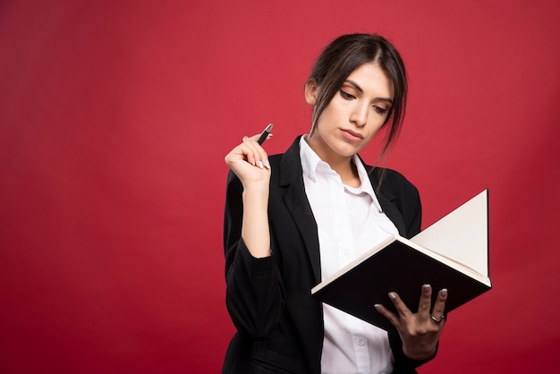 Successful employee reading her memory book on red background. 