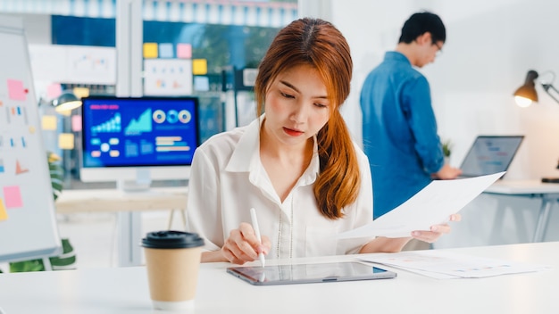 성공적인 임원 아시아 젊은 사업가 스마트 캐주얼 드로잉, 쓰기 및 현대 홈 오피스에서 영감 검색 아이디어 작업 과정의 디지털 태블릿 컴퓨터 생각 펜을 사용하여 착용하십시오.
