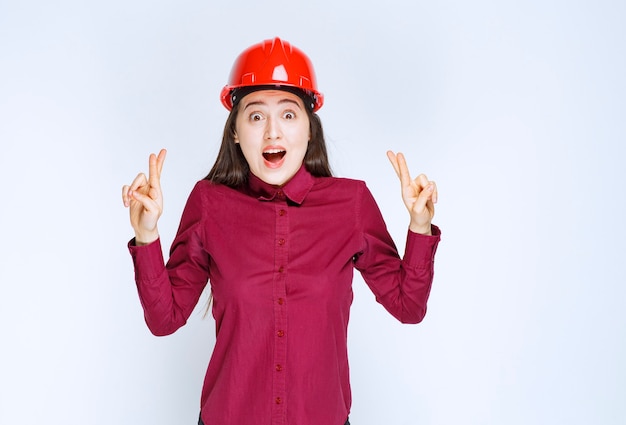 Successful female architect in red hard helmet standing and giving signs. 