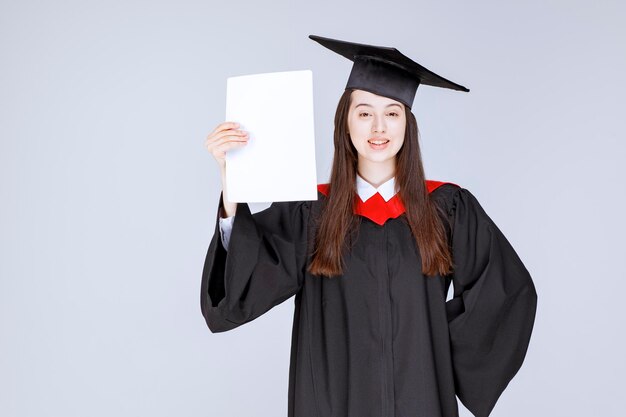 Successful female student paper in hand standing over gray wall. High quality photo