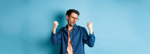 Foto gratuita ragazzo di successo che balla e trionfa con nuovi occhiali alzando le mani in un gesto di pompa a pugno dì di sì a