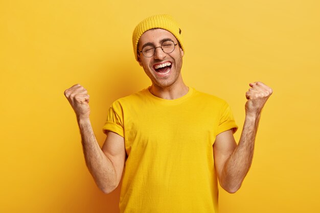 Successful happy young male clenches fists in victory gesture, receieves champion place