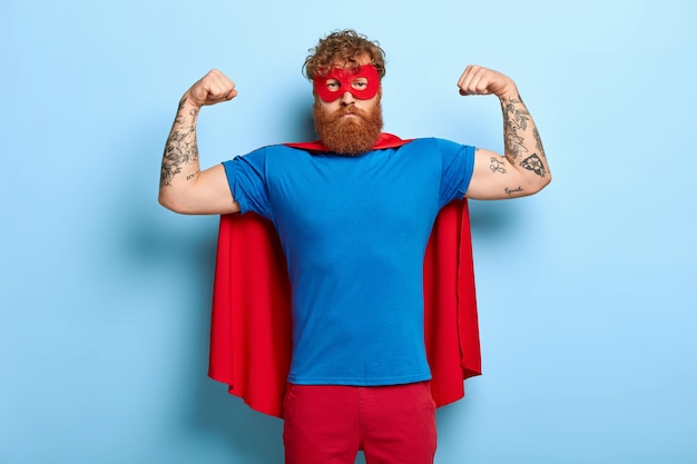 Free photo successful hero wears red mask and cape, raises arms