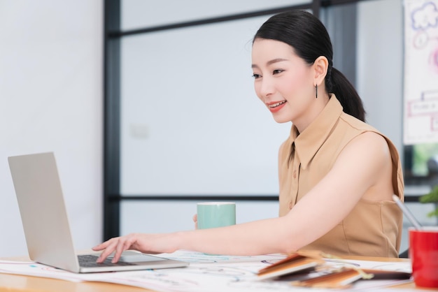 成功したリーダーシップスマート魅力的なアジアの女性は、ラップトップの自信を持って陽気な笑顔のオフィスの背景で働いています