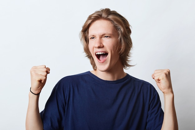 Successful male with happy expression, clenching fists with triumph, rejoicing his success at work. Happy male student being glad to pass exams successfully. People, happiness and joy concept