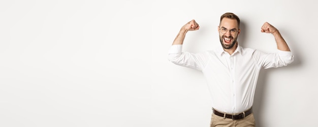 Free photo successful manager flex biceps showing muscles and looking confident standing over white background