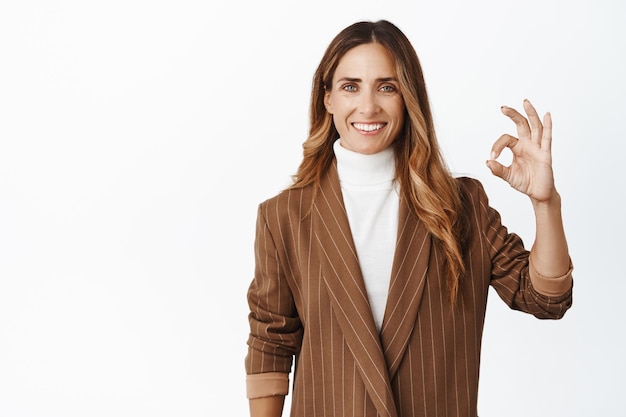 Successful middle aged businesswoman showing ok okay sign and nod in approval smiling pleased approve something good white background