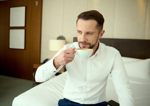 出張中にホテルのアパートでコーヒーを飲むビジネスカジュアルな服装で成功した中年のヨーロッパのビジネスマン。一日の始まりにぴったりの淹れたてのコーヒー