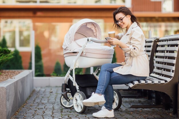 Successful mother with a newborn baby in a stroller drinks tea or coffee in a street near home