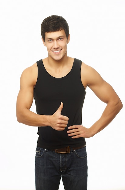 Успешный мускулистый молодой человек показывает большой палец вверх и улыбается