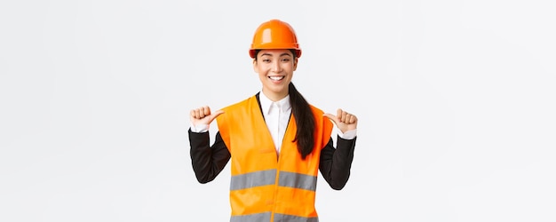 Free photo successful proud smiling asian female construction manager engineer in safety helmet pointing at herself showoff architect recommend personal assistance bragging accomplishments