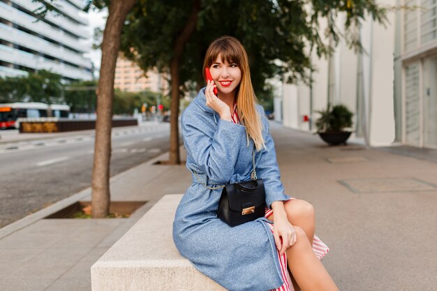 Successful smiling blond female talking by mobile phone in street