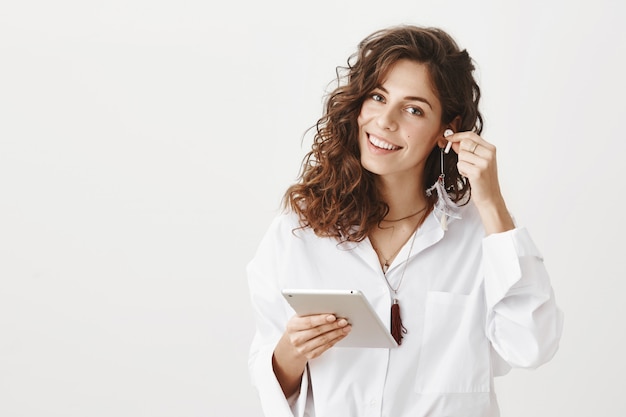 Foto gratuita la donna di affari sorridente riuscita ha messo il trasduttore auricolare senza fili e tiene la compressa digitale