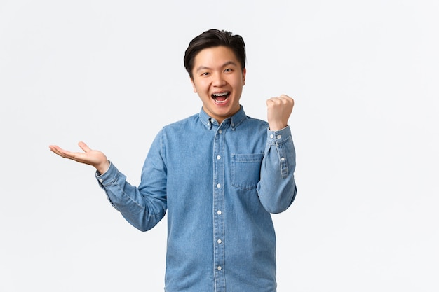 Successful winning asian male freelancer, guy fist pump holding something on hand over black white space, achieve item, receive product he wanted, celebrating or triumphing.
