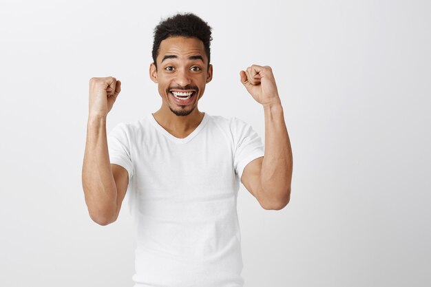 Successful winning dark-skinned guy rejoicing, fist pump and smiling, saying yes, triumphing