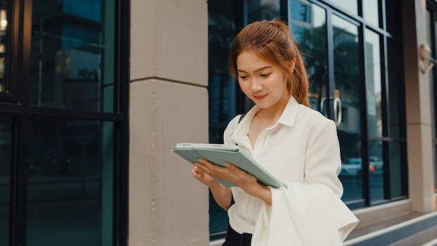 디지털 태블릿을 사용하고 텍스트 메시지를 입력하는 패션 사무실 옷에서 성공적인 젊은 아시아 사업가