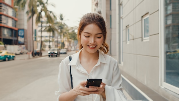 Успешная молодая азиатская коммерсантка в модной офисной одежде с помощью смартфона и ввода текстового сообщения