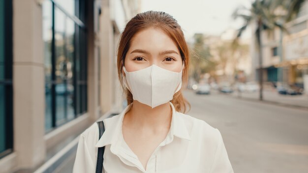 Successful young asian businesswoman in fashion office clothes wearing medical face mask smiling in the street