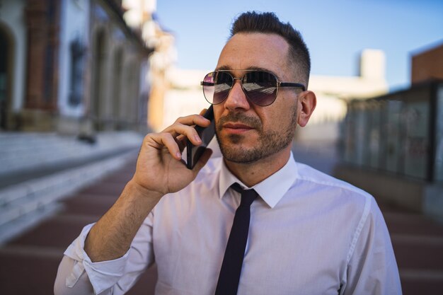 Successful young businessman in a formal outfit with sunglasses talking on the phone