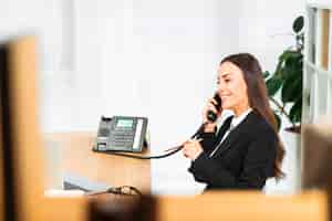 Free photo successful young businesswoman talking on telephone with pencil in hand