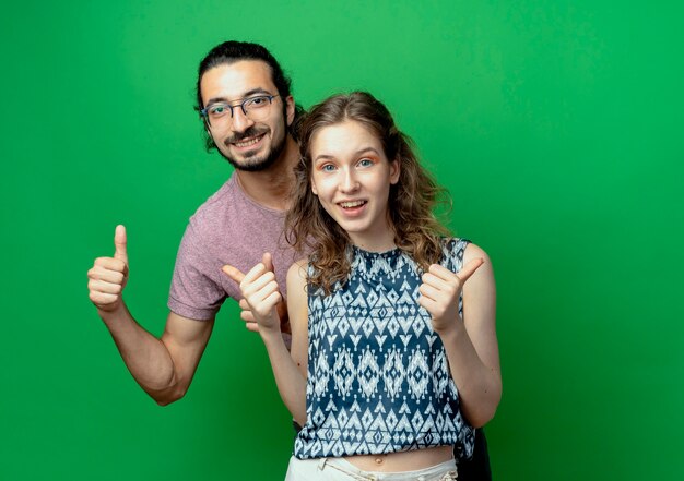 Free photo successful young couple man and woman looking at camera smiling cheerfully showing thumbs up over green background