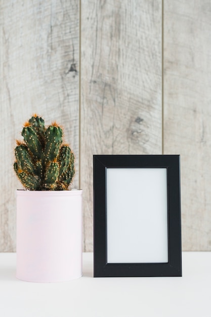 Succulent plant in container near the blank picture frame on desk against wooden wall