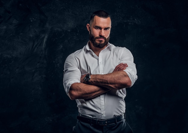 Sucessful bearded businessman in white shirt is posing at dark photo studio.