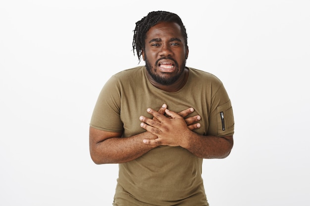 Suffering displeased guy in a brown t-shirt posing against the white wall