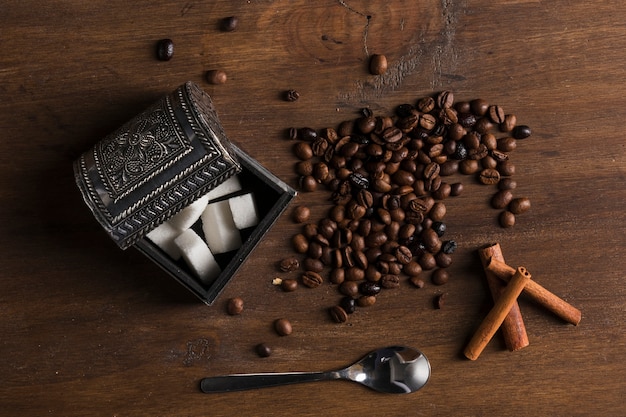 Sugar bowl and coffee beans near cinnamon sticks and spoon