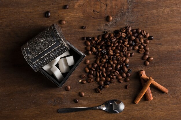 Sugar bowl and coffee beans near cinnamon sticks and spoon