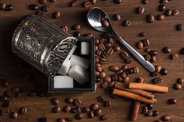 Sugar bowl near cinnamon sticks, spoon and coffee beans