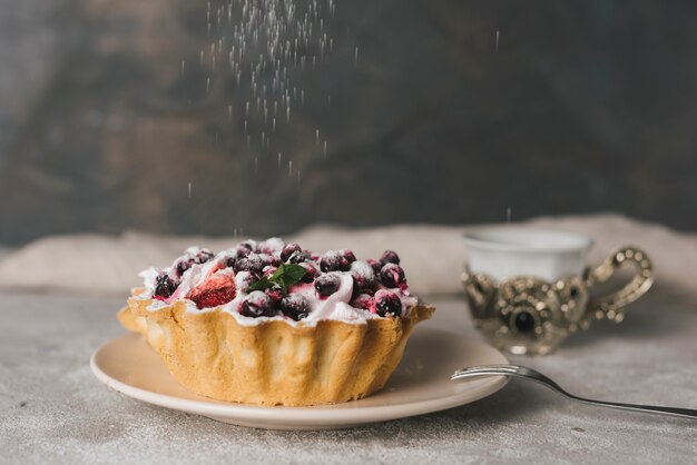 Sugar dusting on fruit tart with berries on ceramic plate