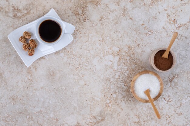 Sugar, ground coffee powder, a cup of coffee and glazed peanuts 