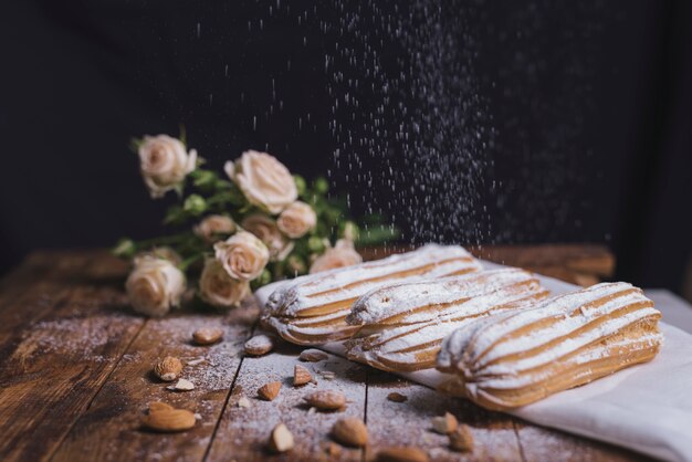 Sugar powder dusted on baked eclairs with almonds on wooden backdrop