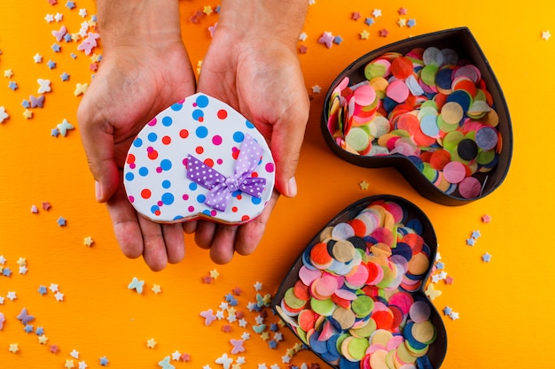 sugar sprinkles, confetti in boxes on yellow table and male holding present box.