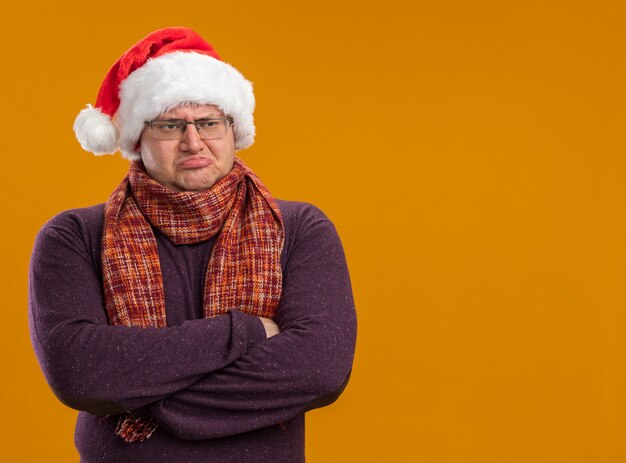 복사 공간 오렌지 배경에 고립 된 측면을보고 닫힌 자세로 목 서 스카프와 안경과 산타 모자를 쓰고 찡그린 성인 남자